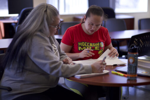 Two Indigenous students from the St'at'imc/Nlaka'pamux and Fort McKay First Nations studying using their notebooks at a campus common space.