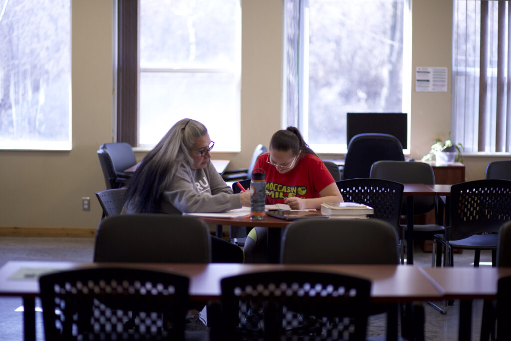 Two Indigenous students from the St'at'imc/Nlaka'pamux and Fort McKay First Nations studying from their notebooks in a campus common space.