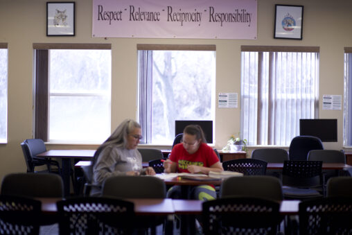 Two Indigenous students from the St'at'imc/Nlaka'pamux and Fort McKay First Nations studying from their notebook notes at a table in a common space on campus.