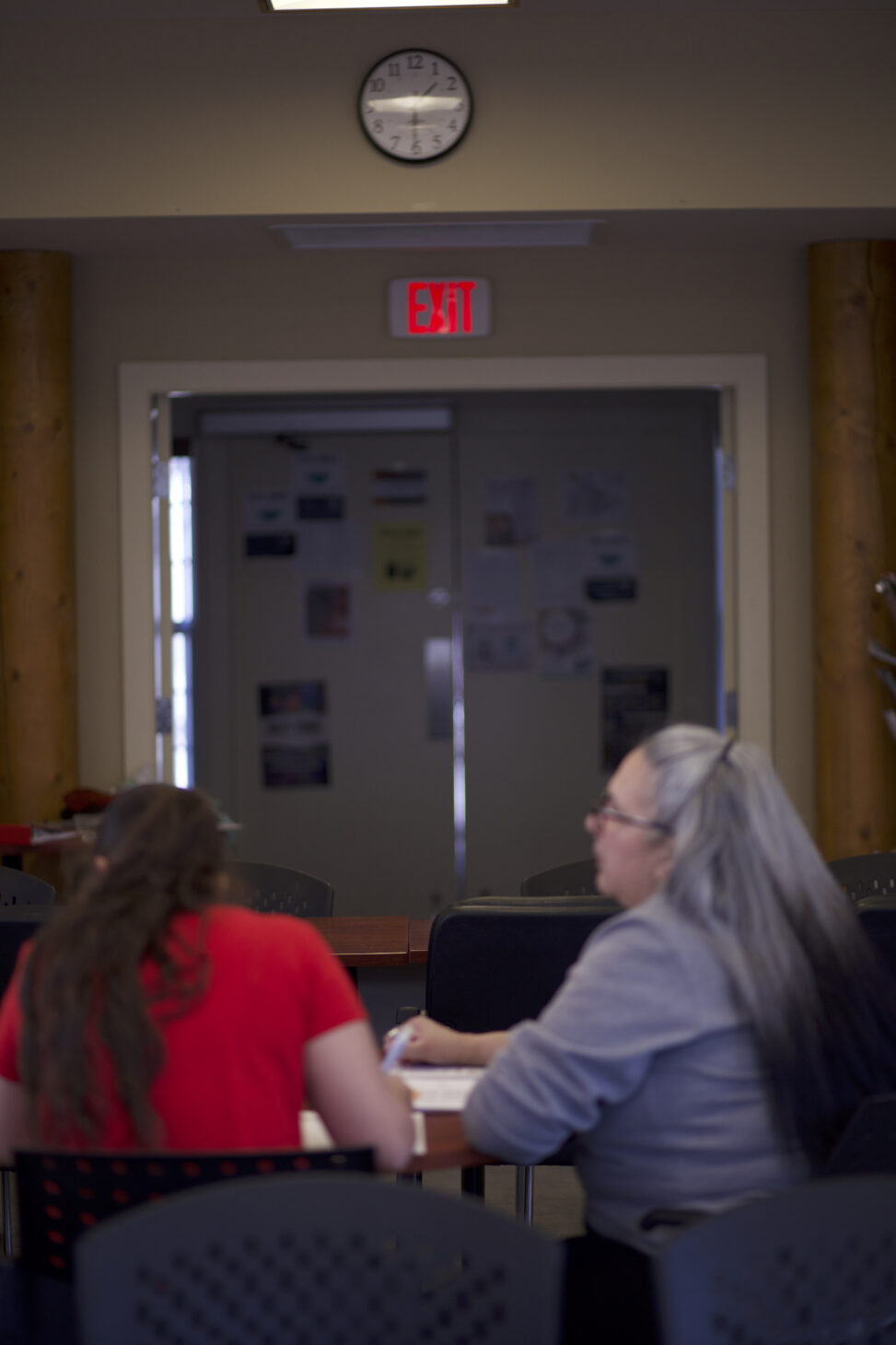 Two Indigenous students from the St'at'imc/Nlaka'pamux and Fort McKay First Nations sitting and studying below a clock in a campus commons space.