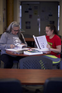 Two Indigenous students from St'at'imc/Nlaka'pamux and Fort McKay First Nations, reading books in a campus common space.