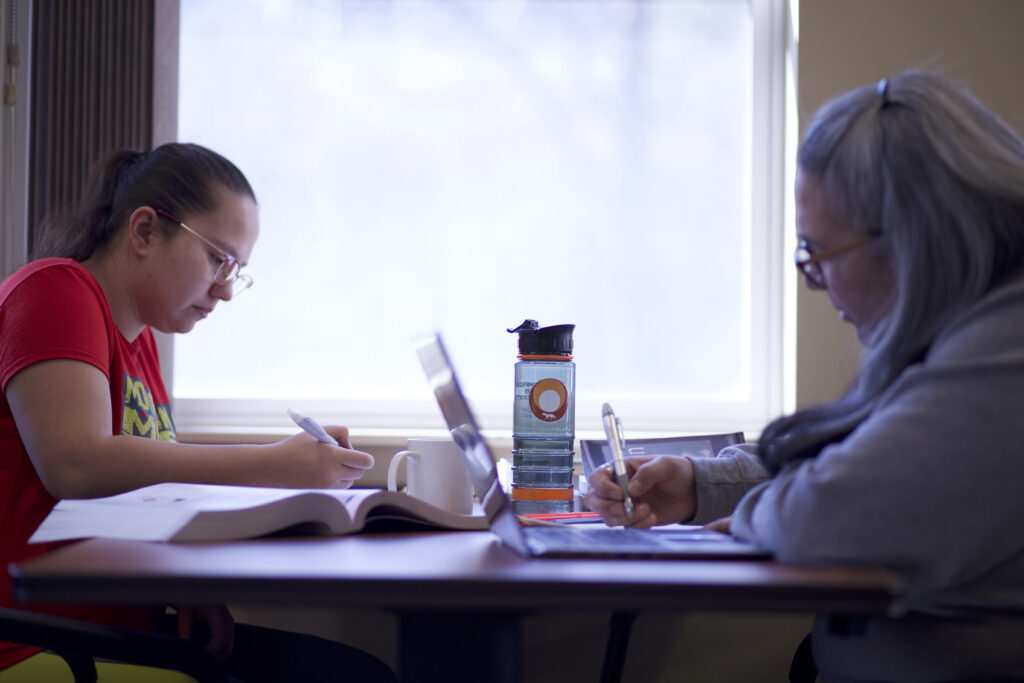 Two indigenous students from the St'at'imc/Nlaka'pamux and Fort McKay First Nations studying and taking notes at a common space on campus.