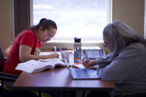 Two Indigenous students from the St'at'imc/Nlaka'pamux and Fort McKay First Nations studying and taking notes at a table in a common space on campus.