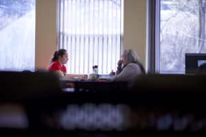 Two Indigenous students from the Stat'imc/Nlakapamux Fort McKay First Nations studying at a table that has a lot of books on it in a campus common space.