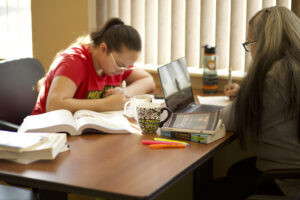 Two Indigenous students from the Stat'imc/Nlakapamux and Fort McKay First Nations studying by taking notes at a table in a campus common space.