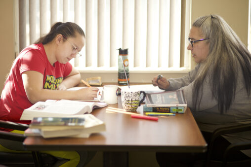 Two indigenous students from the Stat'imc/Nlakapamux Fort McKay First Nations sitting down and taking notes while studying at a common space on campus.