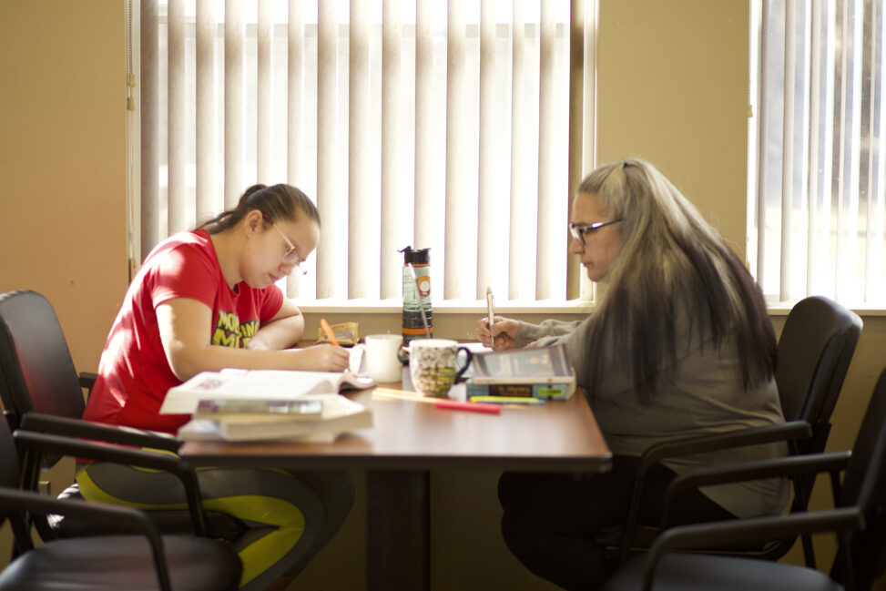 Two Indigenous students from the Stat'imc/Nlakapamux Fort McKay First Nations sitting and studying by taking notes in a campus common space.