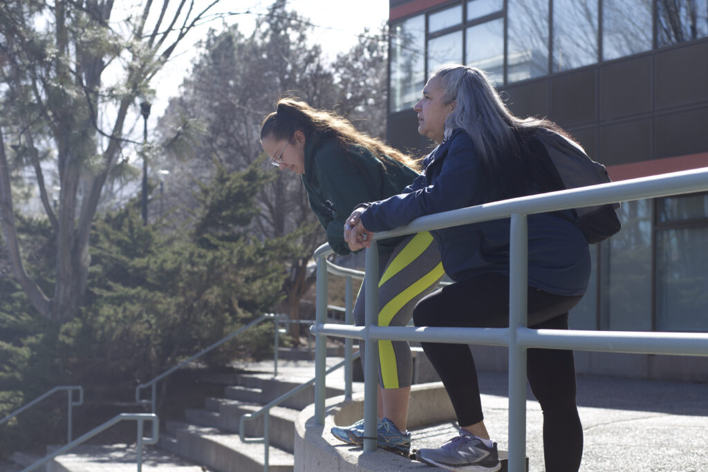 Two indigenous students from the Stat'imc/Nlaka'pamux and Fort McKay First Nations in front of a campus building outdoors.