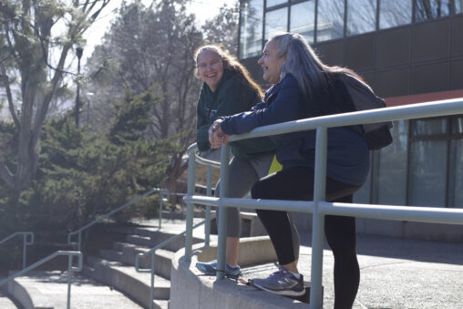 Two Indigenous students from the Stat'imc/Nlaka'pamux and Fort McKay First Nations laughing outdoors in front of a campus building.