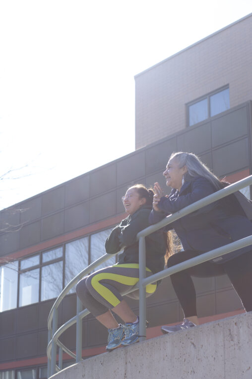 Two indigenous students from the Stat'imc/Nlaka'pamux and Fort McKay First Nations smiling in front of a campus building outdoors.